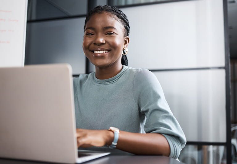 smiling employee seated at table with laptop - staff retention post